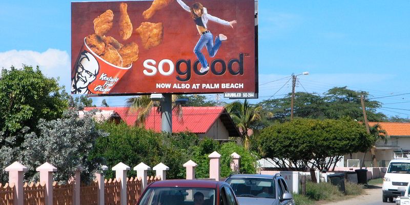 A bigger then life sized billboard next to a busy road with an advertisement for KFC